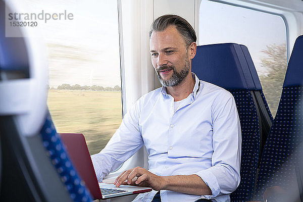 Ein reifer Mann sitzt im Zug und benutzt einen Laptop