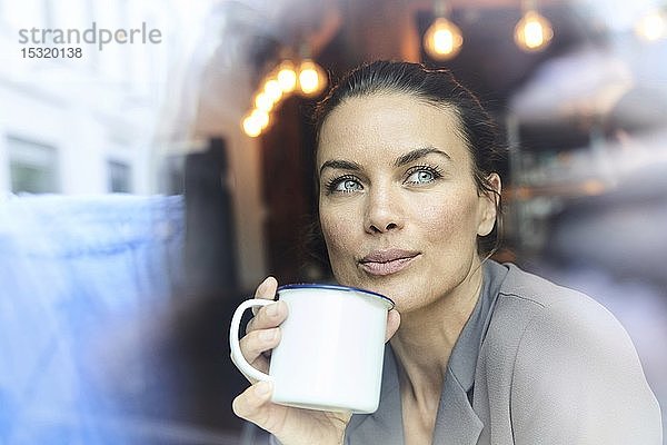 Porträt einer Geschäftsfrau hinter einer Fensterscheibe in einem Café beim Kaffeetrinken