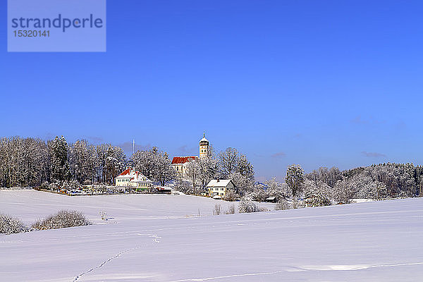 Pfarrkirche St. Johann Baptist in schneebedeckter Landschaft vor strahlend blauem Himmel