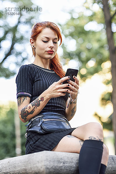 Porträt einer rothaarigen  tätowierten Frau  die ein Mobiltelefon im Freien benutzt
