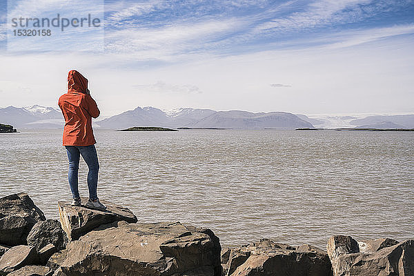 Junge Frau steht auf Felsblöcken und schaut auf das Meer  Südost-Island