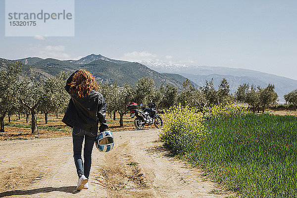 Rückenansicht eines rothaarigen Motorradfahrers auf einem Feldweg  Andalusien  Spanien