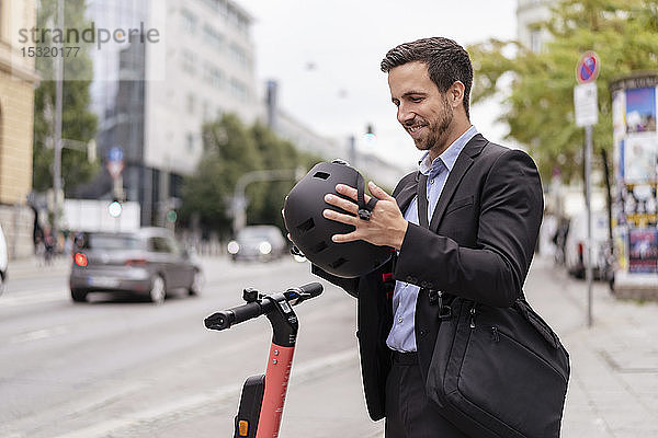 Geschäftsmann mit E-Scooter in der Stadt setzt Helm auf