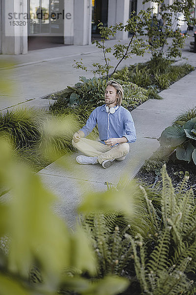 Junger Mann meditiert vor Bürogebäude