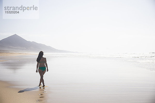 Rückenansicht einer Frau  die bei Ebbe am Strand spazieren geht  Fuerteventura  Spanien