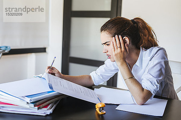 Frustrierte Studentin mit Dokumenten am heimischen Schreibtisch