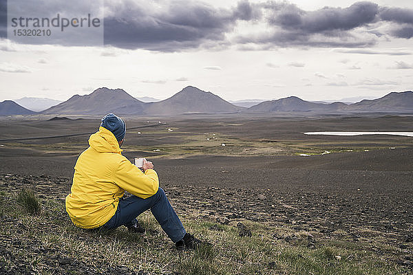 Mann beim Kaffeetrinken  Blick auf Landschaft in Island