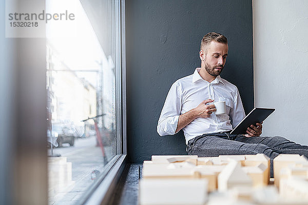Geschäftsmann mit Tablette  Tasse Kaffee und Architekturmodell im Büro