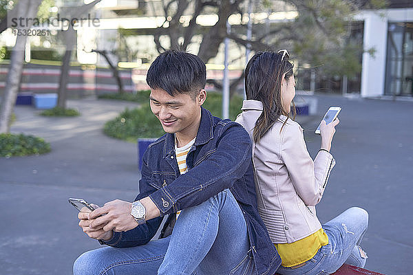 Entspanntes Paar sitzt Rücken an Rücken und benutzt Handys  Barcelona  Spanien