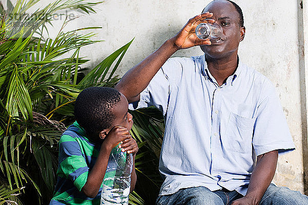 Ein Mann mittleren Alters trinkt Wasser aus einem Glas und ein Kind schaut zu.