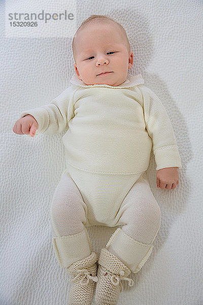 Draufsicht auf ein 2 Monate altes Baby in weißer Bettwäsche  das auf dem Rücken liegt.