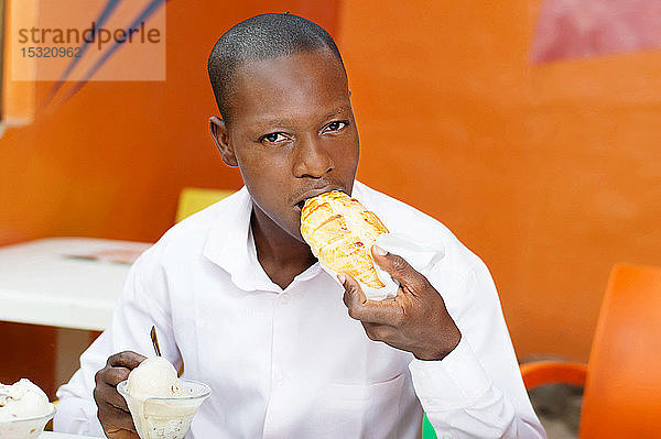 Ein junger Mann sitzt in einem Restaurant und isst sein Brot mit einem Eis.