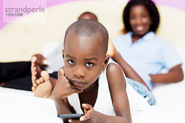 Kind spielt mit dem Mobiltelefon seiner Eltern  die im Hintergrund lächelnd zusehen.