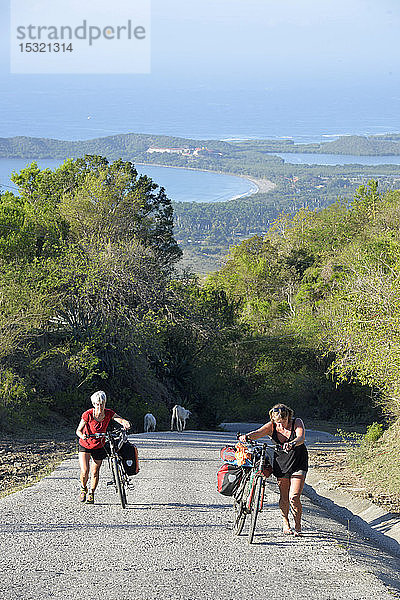 Kuba  östliche Region  2 Radtouristen schieben ihre Fahrräder auf dem Weg nach oben  wir können den blauen Ozean im Hintergrund sehen