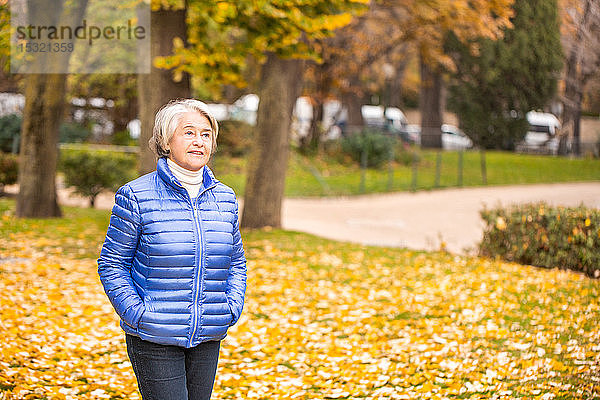 Porträt einer nachdenklichen hübschen älteren Frau  die ruhig durch einen Park vor gelben Blättern geht.
