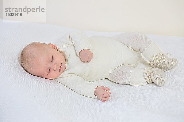 Blick auf einen kleinen Säugling in weißer Kleidung von 2 Monaten  der auf einem weißen Bettchen schläft.