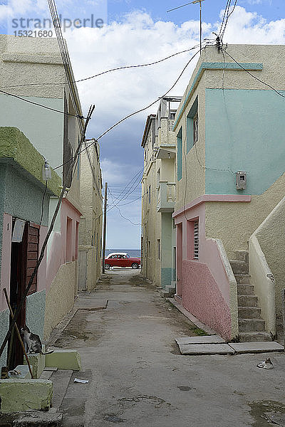 Kuba  Gibara  ein altes rotes amerikanisches Auto aus den 50er Jahren fährt am Ende eines bunten Hauses vorbei
