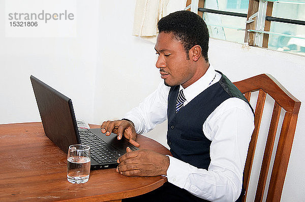 Junger Geschäftsmann sitzt in seinem Büro und arbeitet an seinem Laptop.