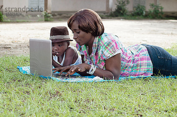 Diese Frau und ihr Sohn liegen im Gras und arbeiten an ihrem Laptop.