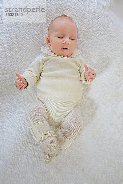 Draufsicht auf einen 2 Monate alten Säugling mit dem Mund im Herzen  der auf einem weißen Bett schläft.