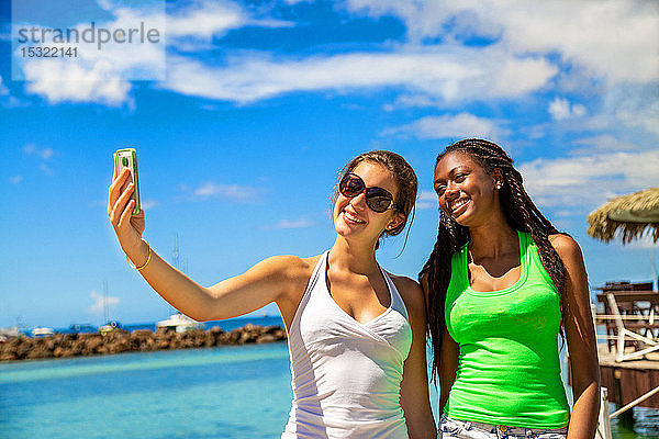 2 lächelnde Mädchen nehmen ein Selfie gegen blauen Himmel Hintergrund.
