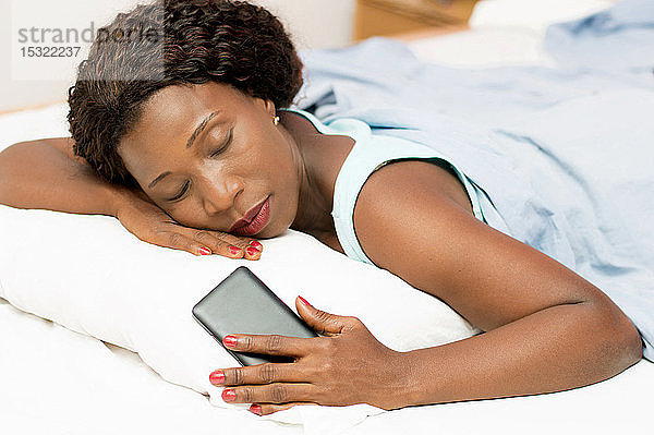 Schöne Frau schläft im Bett mit ihrem Handy in der Hand