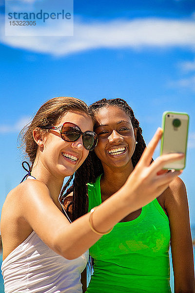 2 lächelnde Mädchen nehmen ein Selfie gegen blauen Himmel Hintergrund.