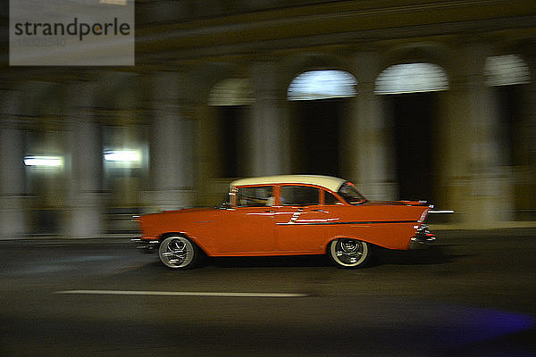 Kuba  La Havanna  ein altes orangefarbenes amerikanisches Auto aus den 50er Jahren fährt nachts mit voller Geschwindigkeit