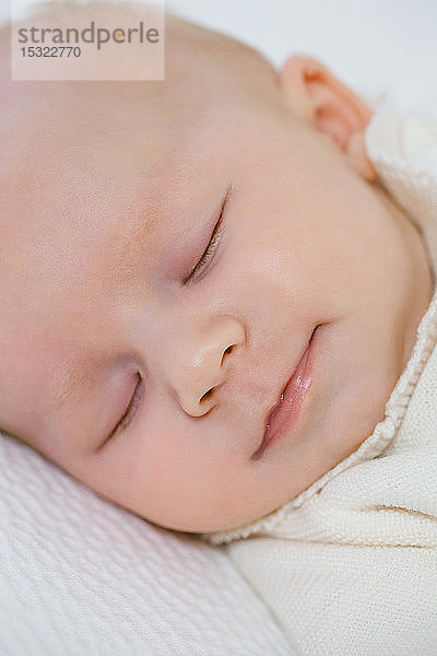 Lächelndes Gesicht eines 2 Monate alten Babys  das auf dem Rücken in seinem Bett schläft.
