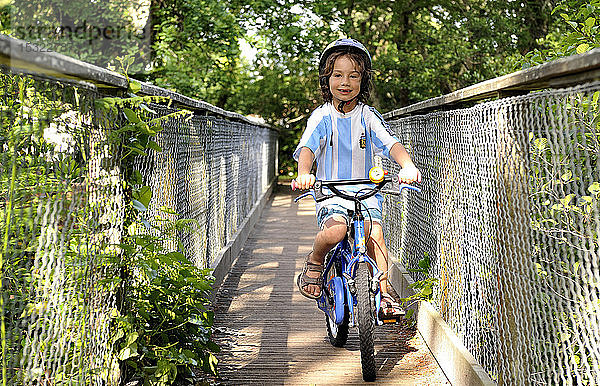 Sechsjähriger Junge radelt auf einer Brücke im Wald