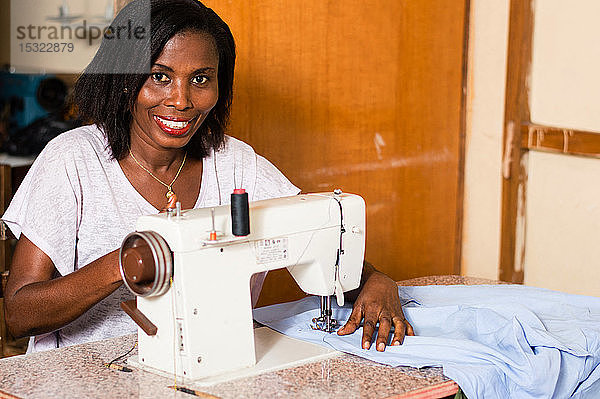 Junge afrikanische Frau  die lächelnd in ihrem Atelier näht  in der Stille.