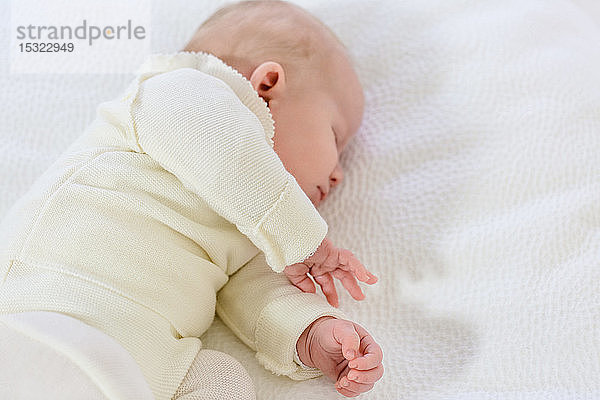 Kleiner Säugling in weißer Kleidung von 2 Monaten schläft auf einem weißen Bett.