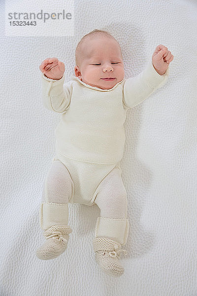 Draufsicht auf ein 2 Monate altes Baby in weißer Kleidung  das auf dem Rücken liegt und mit den Armen wedelt.