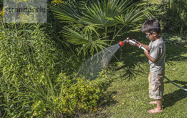 Fünfjähriger Junge beim Gießen der Pflanzen mit einem Schlauch