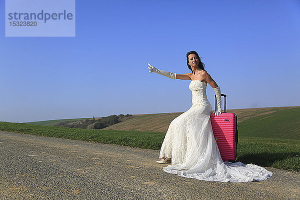 Braut trampen mit rosa Koffer