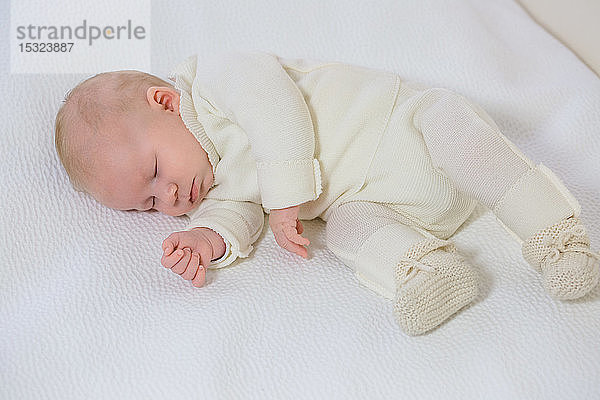 Blick auf einen kleinen Säugling in weißer Kleidung von 2 Monaten  der auf der Seite auf einem weißen Bett schläft.