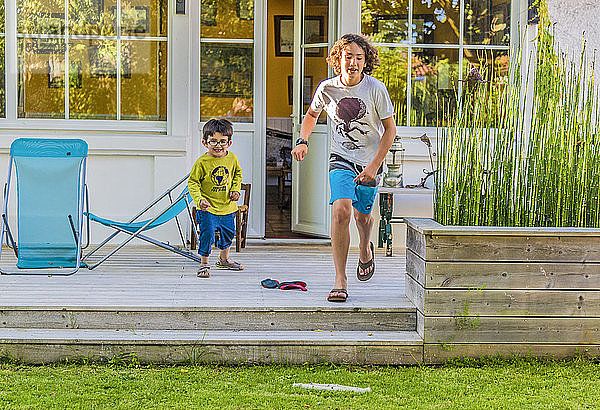 Zwei Jungen im Alter von fünf und dreizehn Jahren rennen aus dem Haus in Richtung Garten