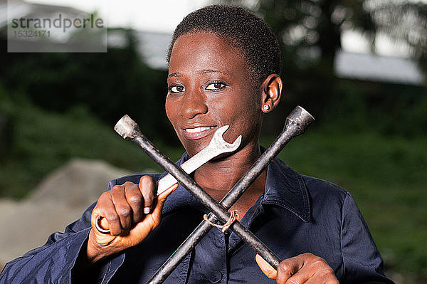 Junge lächelnde Mechanikerin zeigt ihre Werkzeuge in ihrem Freiluftatelier.