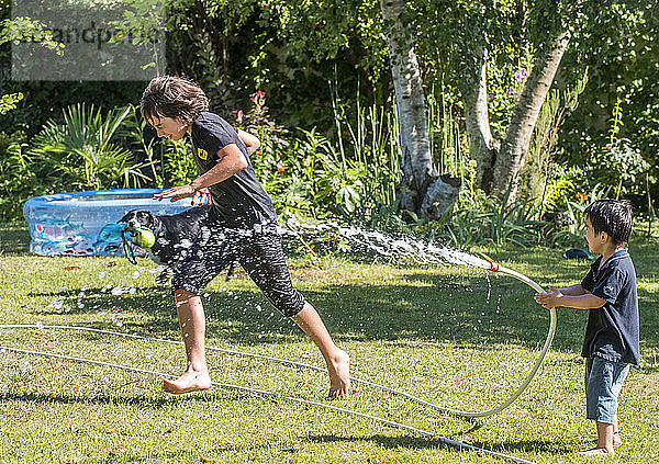 Zwei Jungen im Alter von 4 und 12 Jahren spielen mit einem Schlauch im Garten