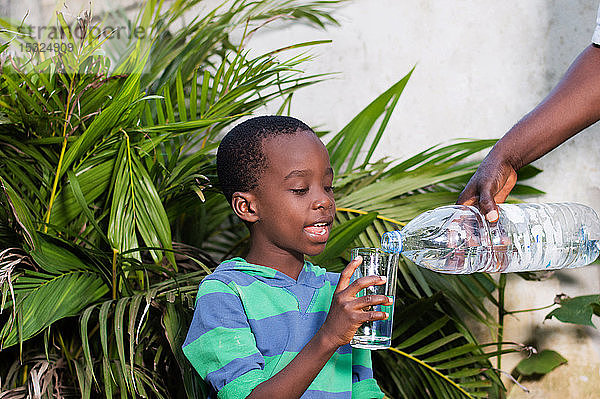Lächelnder kleiner Junge mit einem Wasserglas in der Hand  in dem man ihm Wasser serviert.