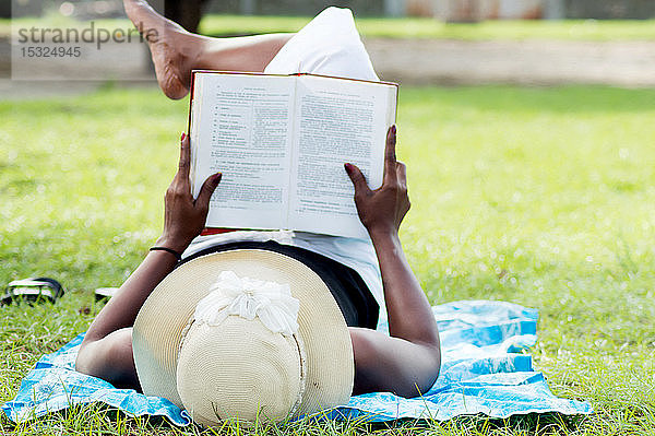Diese junge Frau liegt im Schatten eines Baumes und liest in aller Ruhe.