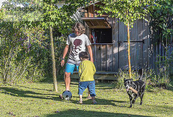 Zwei Jungen im Alter von fünf und dreizehn Jahren spielen mit einem Ball im Garten