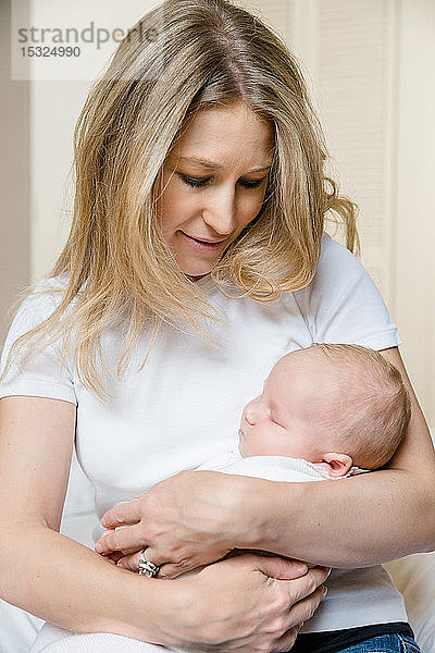 Hübsche junge Mutter  die zärtlich ihr 2 Monate altes Baby in ihren Armen hält.