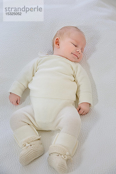 Draufsicht auf einen kleinen Säugling  der auf einem weißen Bett schläft.