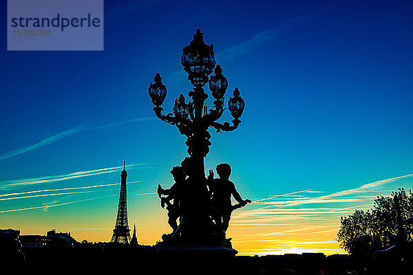 Frankreich  Paris  Pont Alexandre III  5. Oktober 2018: Sonnenuntergang auf dem Eiffelturm  von einem Laternenpfahl und Statuen 'Runde Liebe'