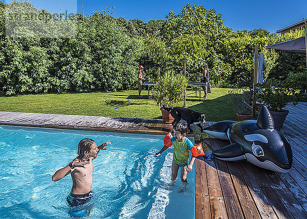 Zwei Jungen im Alter von 5 und 13 Jahren spielen im Schwimmbad  im Hintergrund spielt eine Mutter mit ihrer Tochter Tischtennis.