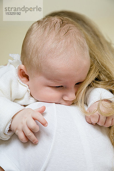 Nahaufnahme eines 2 Monate alten Babys auf der Schulter seiner Mutter.