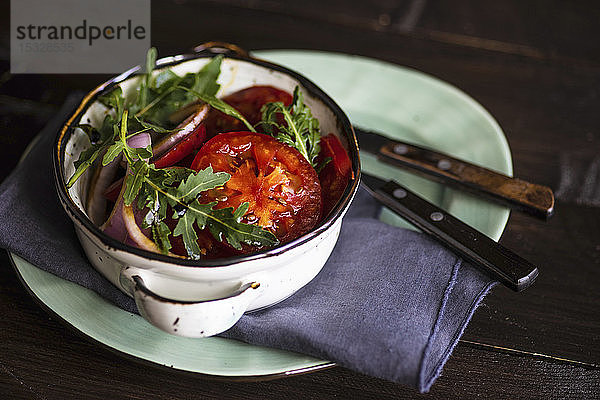 Keramikschüssel mit Salat aus Bio-Gemüse wie einer Tomate  roten Zwiebeln  Rucola und Leinsamen