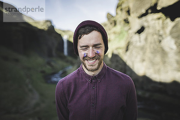 Lächelnder Mann mit Blumen im Gesicht am Kvernufoss-Wasserfall in Island