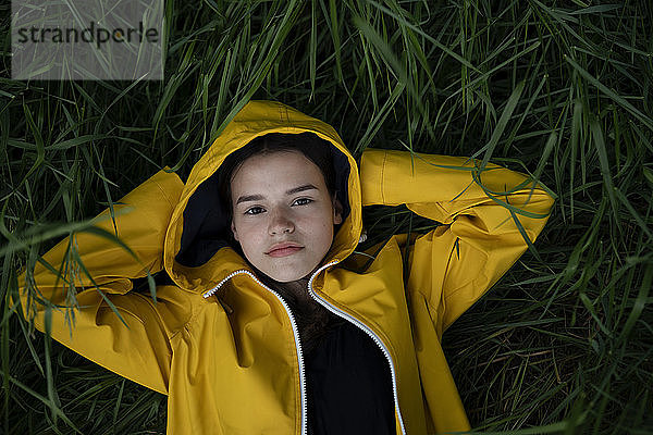 Jugendliches Mädchen mit gelbem Regenmantel im Gras liegend